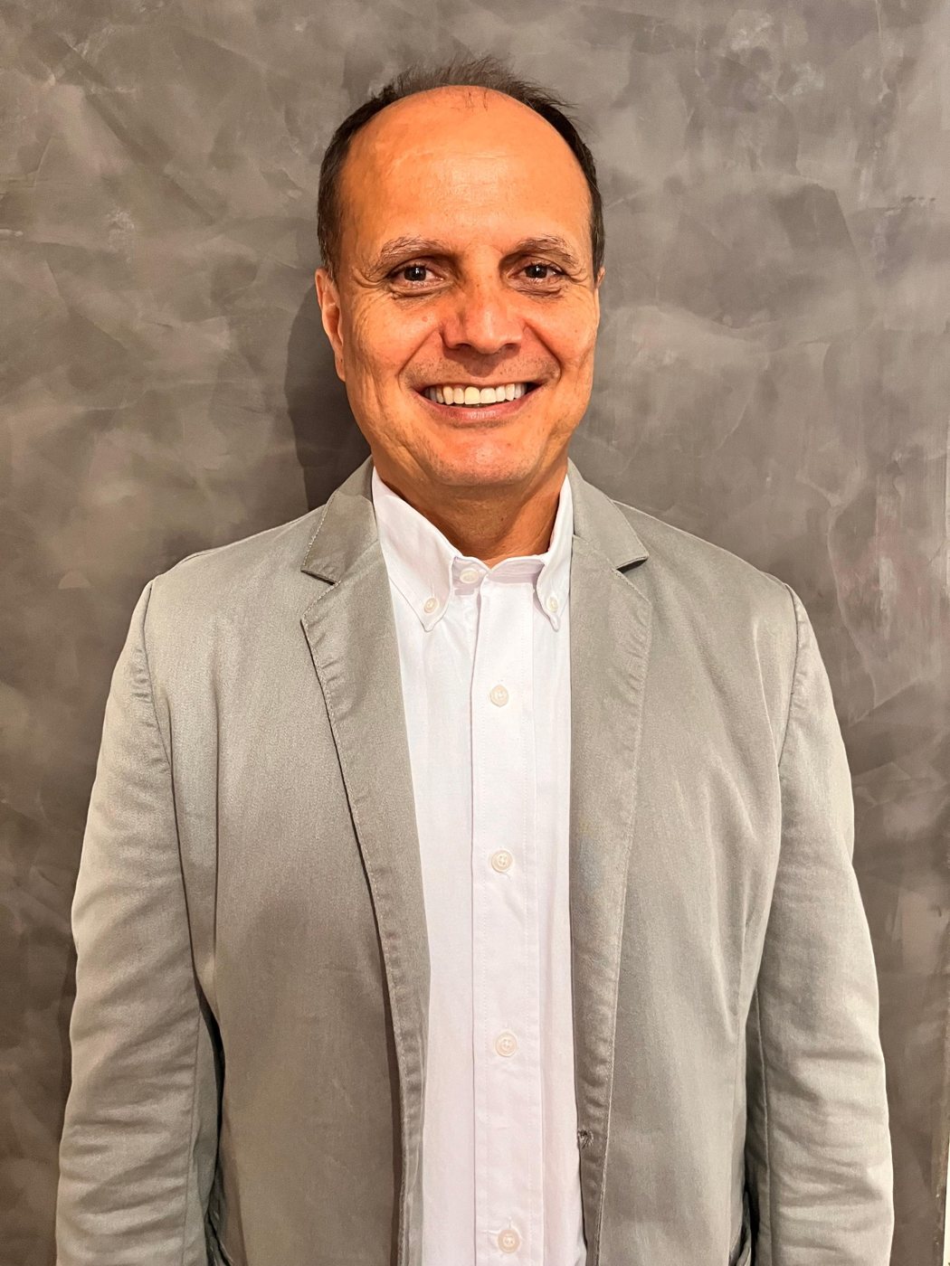 Professor Magno sorrindo, de blazer cinza e camisa branca